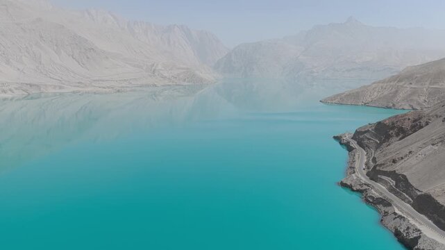 Aerial view of the turquoise Baisha Lake contrasting with the muted tones of the surrounding mountains and road, Baisha Lake, Xinjiang, China.