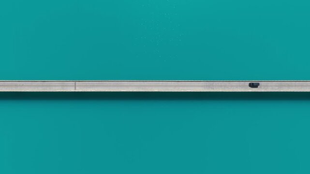 Aerial view of a car traveling across a gray bridge spanning the turquoise waters of Baisha Lake, creating a vivid contrast, Baisha Lake, China.