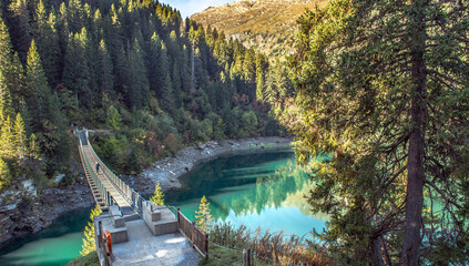 metal walkway crossing a beautiful Saint Guerin alpine lake encased in the mountain  with forest