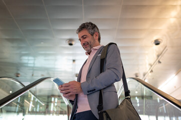 Businessman using phone on escalator in modern airport