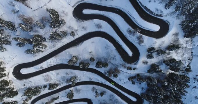 Aerial view of a winding road snaking through a snowy, mountainous landscape, contrasting dark asphalt with the pristine white snow, Maloja Pass, Grisons, Switzerland.