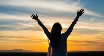Silhouette of a woman with arms raised triumphantly against a stunning sunset sky. Golden and orange hues paint the horizon while soft clouds drift overhead. Perfect for success concepts.