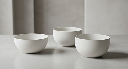 Three minimalist white ceramic bowls arranged on a neutral surface