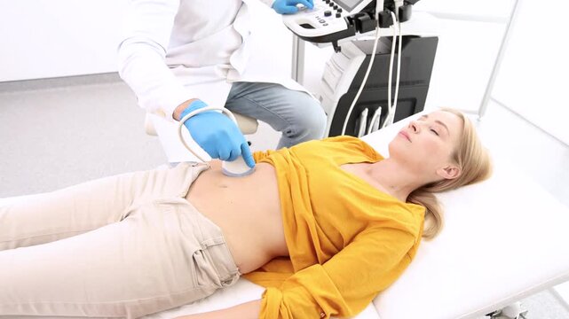 Ultrasound specialist doing ultrasonography of abdominal cavity for female patient with ultrasound machine at hospital