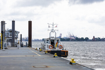 Fototapeta premium Small patrol boat moored at harbor pier with industrial port cranes in background