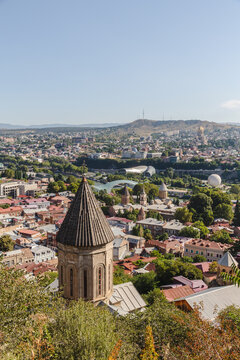 View of a historic stone tower rises above a sprawling cityscape, its aged texture contrasting with the modern buildings, under a vast blue sky, Tbilisi, Tbilisi, Georgia.