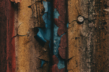 Weathered metal surface with peeling paint in vibrant colors. Close-up of a textured metal surface with layers of yellow, brown, blue peeling paint in various colors, showcasing age and decay.