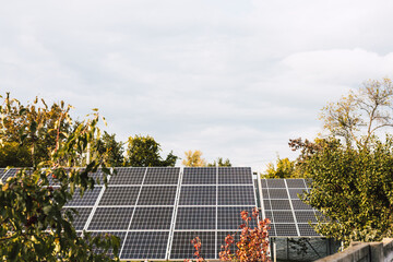 Solar panels installed on a rooftop, generating clean energy. A view of solar panels on a rooftop, surrounded by trees, under a cloudy sky, promoting renewable energy and sustainability.