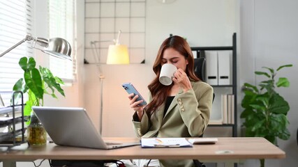Focused Asian businesswoman writing on report paper while working on laptop at home office desk. Modern business planning, research, and productivity concept. - Powered by Adobe