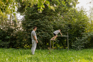 In a serene natural setting, a father watches his son climb on a playground structure. They enjoy this playful moment together, highlighting the joys of parenting and outdoor fun