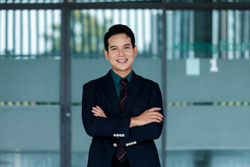 Smiling Asian businessman portraying confidence and success, standing with folded arms in a modern...