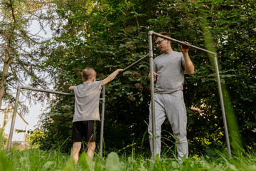 A father and his young son are having fun together at a playground in a lush green park. They are engaged in play, strengthening their bond through enjoyable activities outdoors