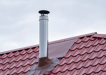 Metal chimney rising from a red roof on a cloudy day in a suburban area © denklim