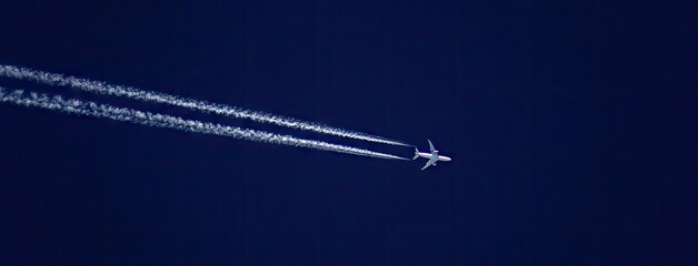 Airplane flying high above clear blue sky leaving white contrails behind during daylight hours