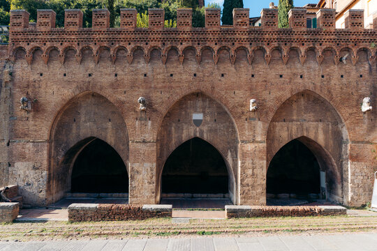 View of the Fonte Branda, a medieval fountain with three archways and a brick facade, standing as a testament to history, Siena, Tuscany, Italy.