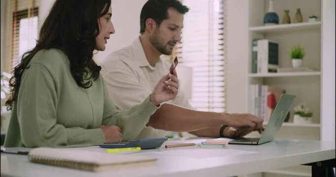 Young couple using credit card for online payment on laptop. Financial planning, budgeting, and ecommerce concept in cozy home workspace with natural light.