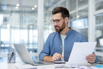 Obraz premium Man working with laptop and documents in modern office