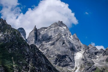 Dramatic Rocky Mountain Peaks with Cliff Faces Against Blue Sky and White Clouds in Alpine Wilderness