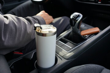 Driver in a car, close-up of manual gear shift lever, white travel mug in cup holder, leather...