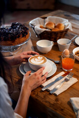 Italian breakfast in an old farmhouse or B&B. Cappuccino with latte art, cake, orange juice. Warm and cozy atmosphere, wooden table.