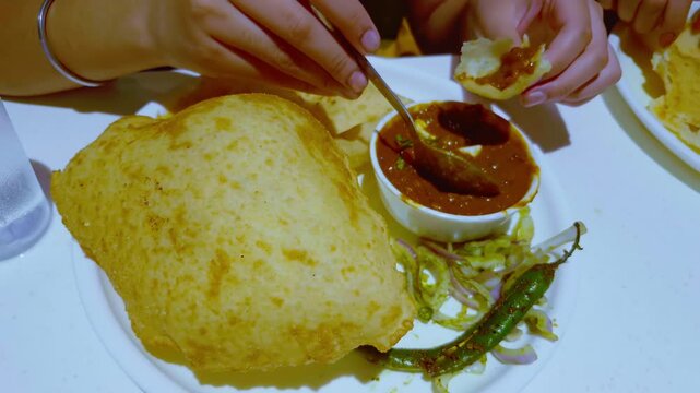 A woman enjoys a traditional meal of Bhature with chole served in a plate and bowl, highlighting classic flavors.