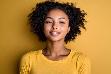 Joyful young adult woman with beautiful afro hairstyle smiling brightly in a vibrant yellow studio