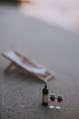 Wine glasses and a bottle of wine on the beach. A miniature wine bottle and two glasses of red wine sit on a sandy beach, with a blurred beach chair in the background.