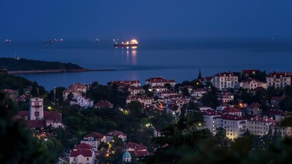 Coastal town overlooking calm sea with ships at twilight blue hour