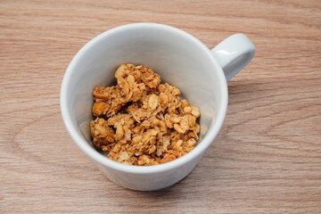 Nutritious and crunchy granola mix presented in a pristine white ceramic mug, offering a wholesome and energetic option for a healthy breakfast or a delightful midday snack on a natural wooden surface