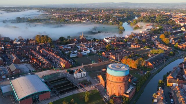 Aerial sunrise video of Chester with mist over the River Dee, terraced housing, and water tower.