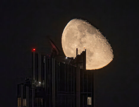 Aerial view of the moon rising behind a tall building, its facade illuminated by a soft glow against the dark sky, New York, New York, United States.