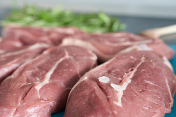 Raw beef steaks on a cutting board with rosemary and salt, close-up.