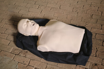 CPR dummy lying dark fabric case, simulating life saving emergency response with an open mouth expressing distress. This educational tool is used for training medical professionals and first