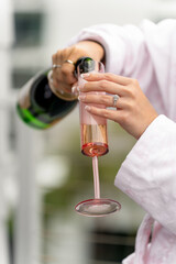 Close-up of woman's hands pouring sparkling wine into a champagne glass. Bride or bridesmaid pouring champagne into a pink glass. Relaxing festive atmosphere at a bachelorette party or birthday