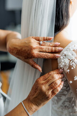 Close-up of a bride getting ready as hands with intricate henna patterns adjust the delicate...