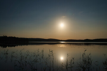 Sunrise at the lake with reeds and forest reflections in golden morning light