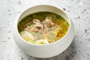 Clear chicken noodle soup with boiled egg slices, fresh herbs, and golden broth in a white bowl on a speckled countertop. Homemade comfort food, top view, close-up