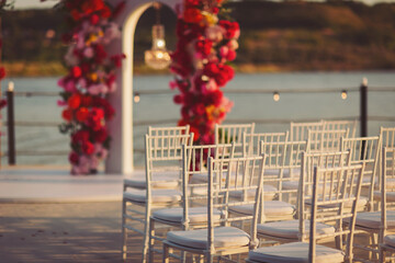 Beautiful wedding setup by the water with elegant chairs and vibrant floral decorations at sunset