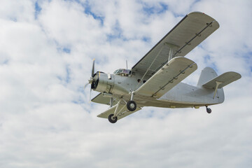 large grey an 2 biplane with a propeller engine flying in a cloudy sky, vintage aircraft in flight, concept of agriculture, cargo transport, retro travel