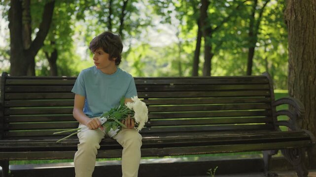 Sad teen boy waiting for girlfriend with flowers, leaving bouquet after no-show