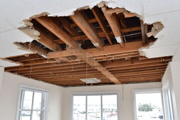 Fototapeta premium A room with a severely damaged ceiling revealing exposed wooden joists and beams, indicating ongoing renovation or structural damage.