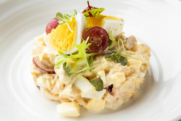 Gourmet salad with chopped eggs, red grapes, creamy dressing, and microgreens, artfully plated on a white dish. Top view, cold appetizer, elegant presentation.