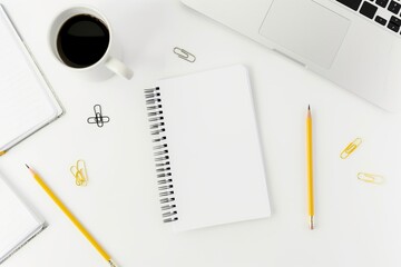 Top view of notepad, pencils, paper clips, and coffee cup on white table, clean school workspace mockup.
