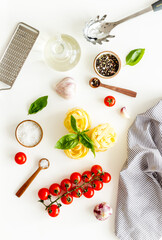 Fettuccine with ingredients for cooking pasta - tomatoes and basil with garlic - on a white background, top view. Flat lay