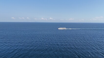 Obraz premium A peaceful scene of a small boat sailing on calm blue sea under clear sky. Gentle waves sparkle in the sunlight, creating a serene and relaxing atmosphere. Ideal footage for travel videos, nature bac