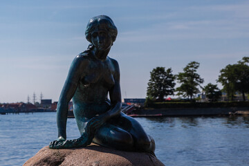 Obraz premium Copenhagen, Denmark 07-20-2025 The bronze statue of the Little Mermaid sitting on a rock by the waterside at the Langelinie promenade in Copenhagen. The small and unimposing statue is an icon in town.