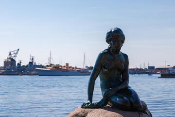Obraz premium Copenhagen, Denmark 07-20-2025 The bronze statue of the Little Mermaid sitting on a rock by the waterside at the Langelinie promenade in Copenhagen. The small and unimposing statue is an icon in town.