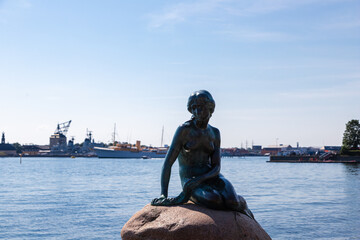Obraz premium Copenhagen, Denmark 07-20-2025 The bronze statue of the Little Mermaid sitting on a rock by the waterside at the Langelinie promenade in Copenhagen. The small and unimposing statue is an icon in town.