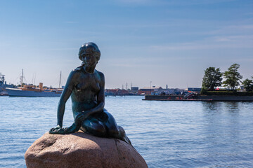 Obraz premium Copenhagen, Denmark 07-20-2025 The bronze statue of the Little Mermaid sitting on a rock by the waterside at the Langelinie promenade in Copenhagen. The small and unimposing statue is an icon in town.