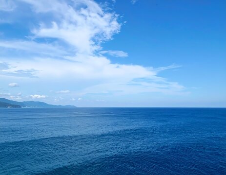 Serene coastal vista; blue ocean meets a clear sky with wispy clouds - Powered by Adobe